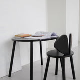 A minimalist black oval desk paired with a matching black chair in a bright, modern room with white walls and a gray floor.