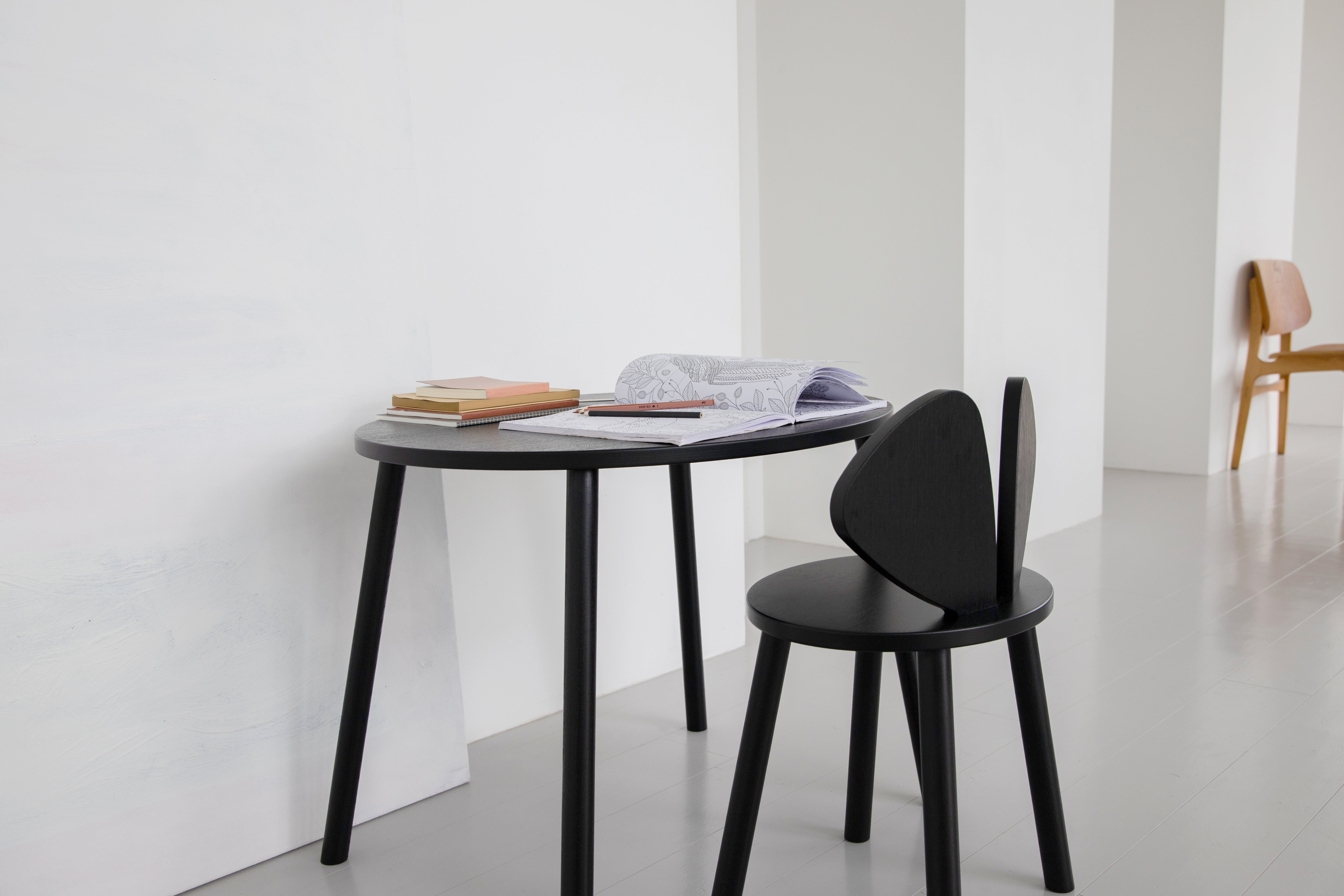 A minimalist black oval desk paired with a matching black chair in a bright, modern room with white walls and a gray floor.