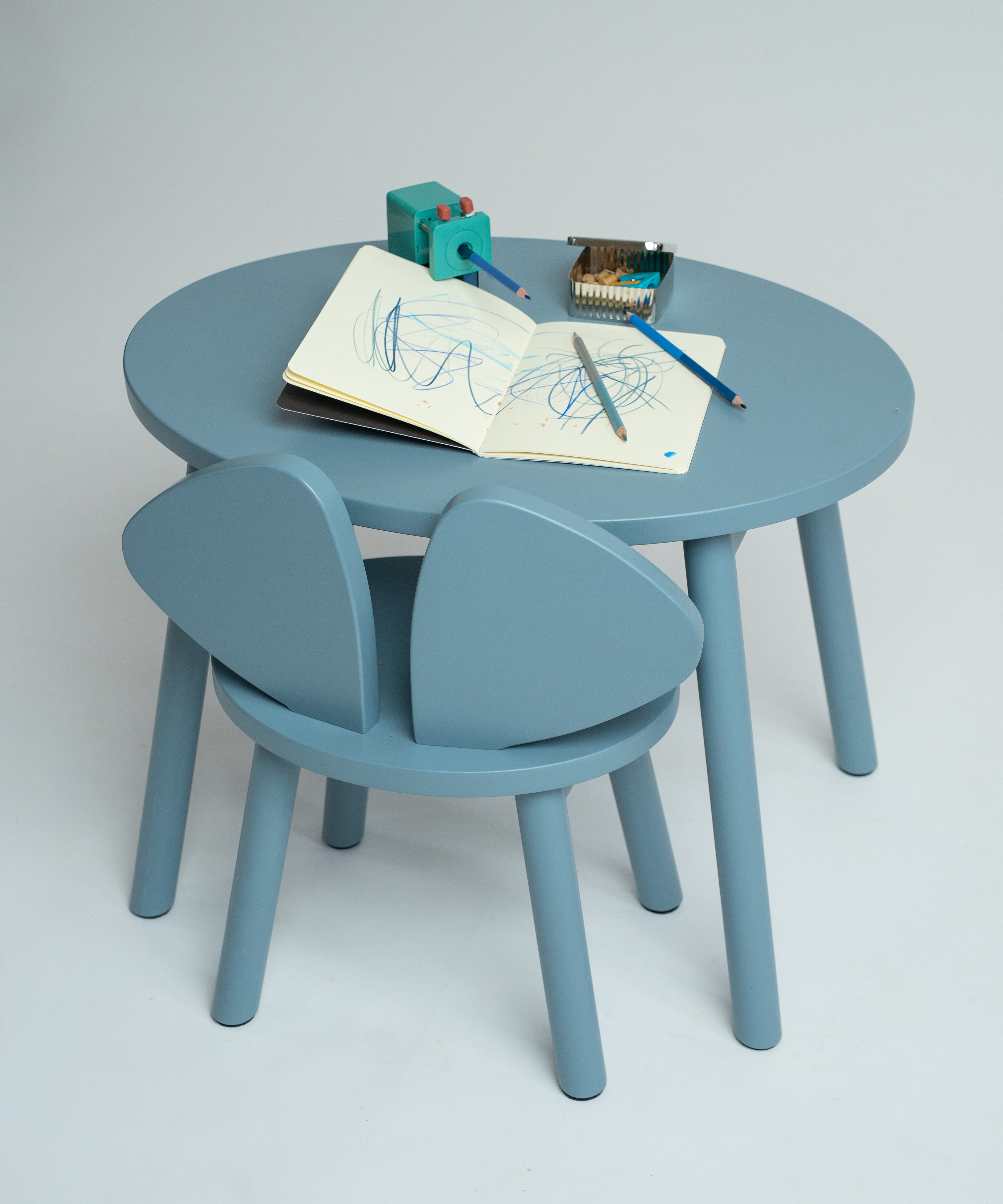 A light blue children's table and chair set with a round table and two matching chairs, styled with drawing accessories on a neutral studio background.