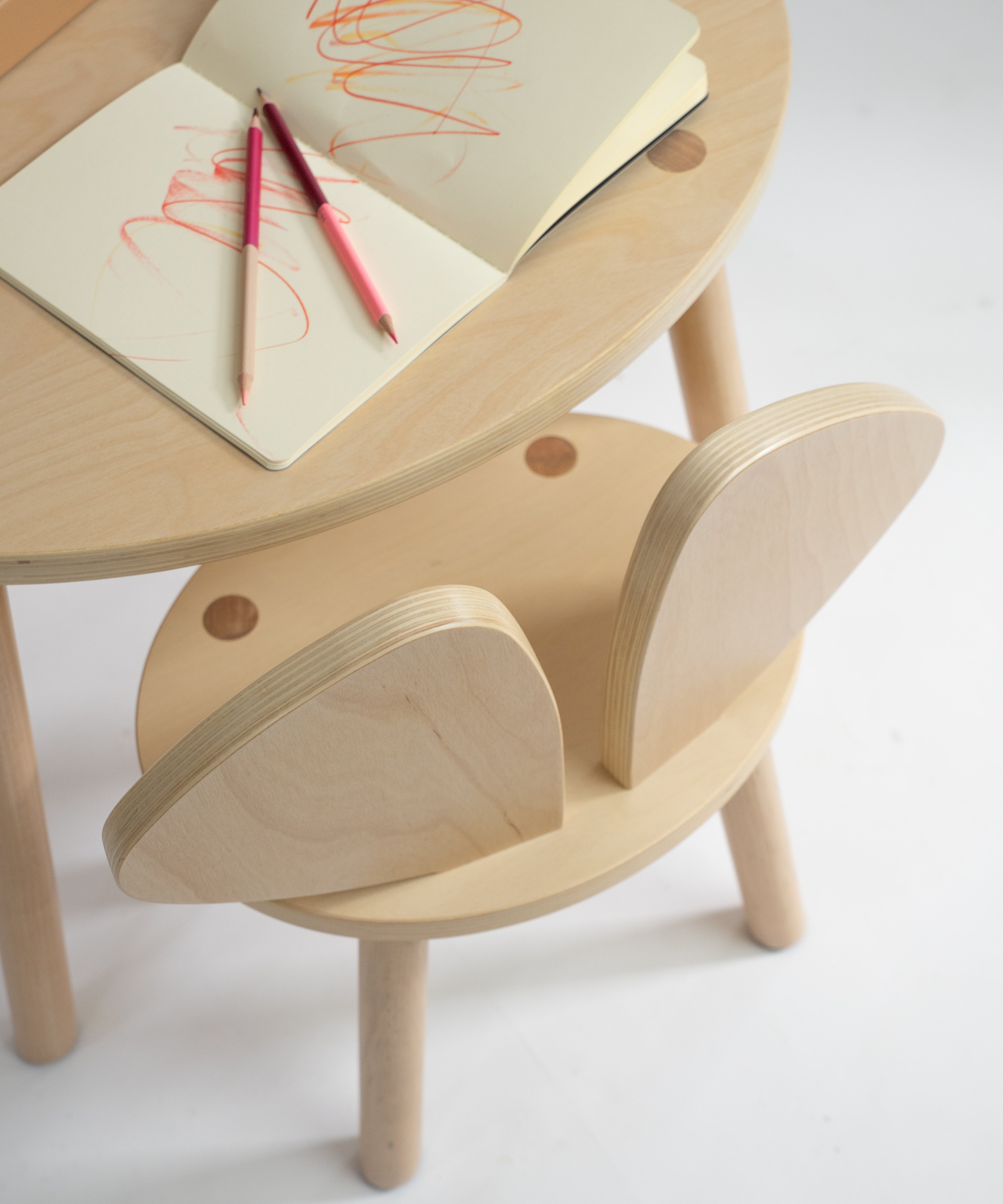 Wooden children's table and chair set with notebooks and pencils on a white background