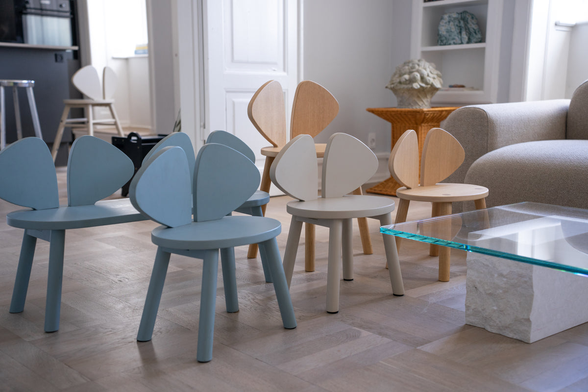 A set of modern wooden chairs with heart-shaped backrests in light blue, cream, and natural wood finishes, arranged in a bright, contemporary living room.