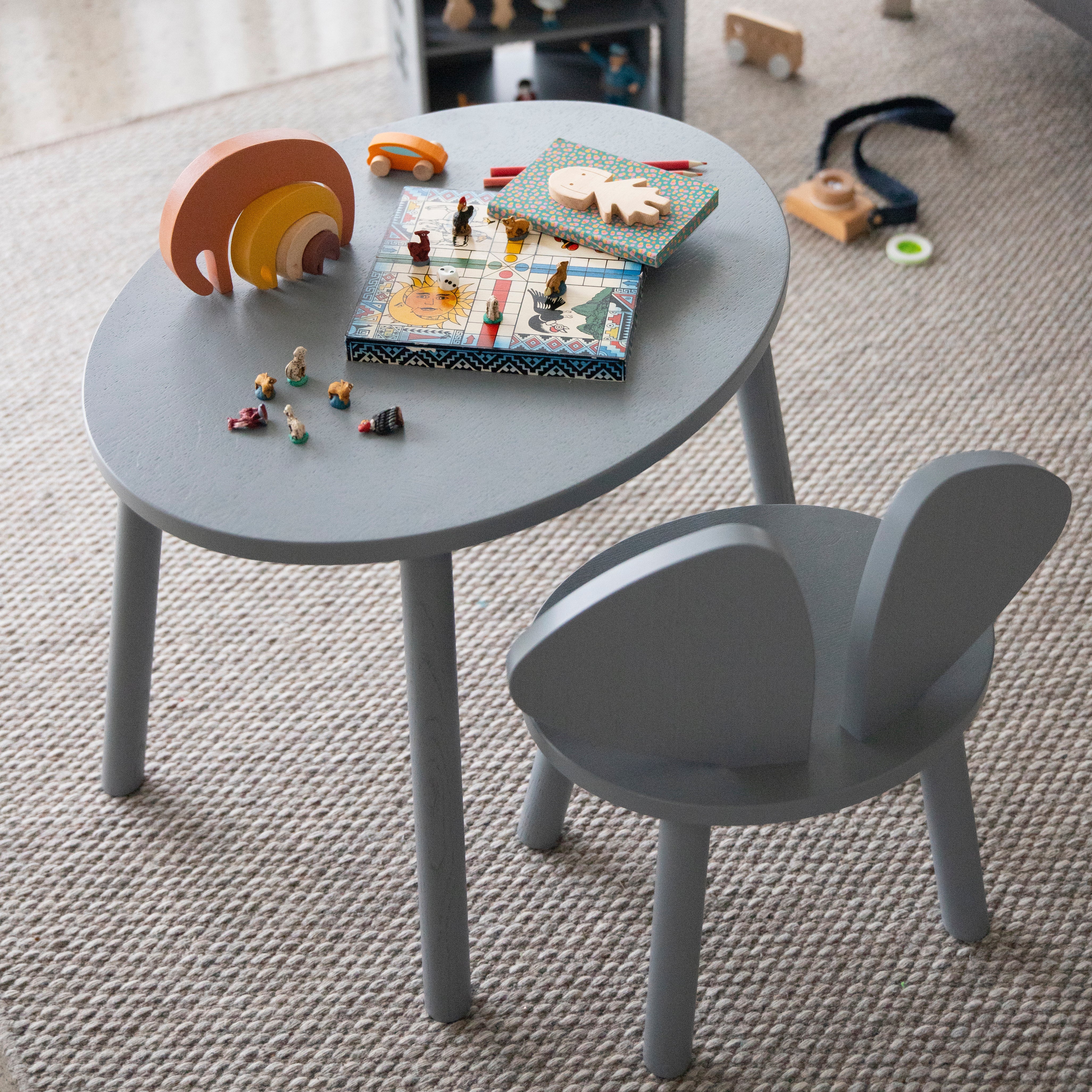 A children's round gray table and matching bunny-shaped chair set on a textured beige rug, styled with wooden toys in a bright indoor room.