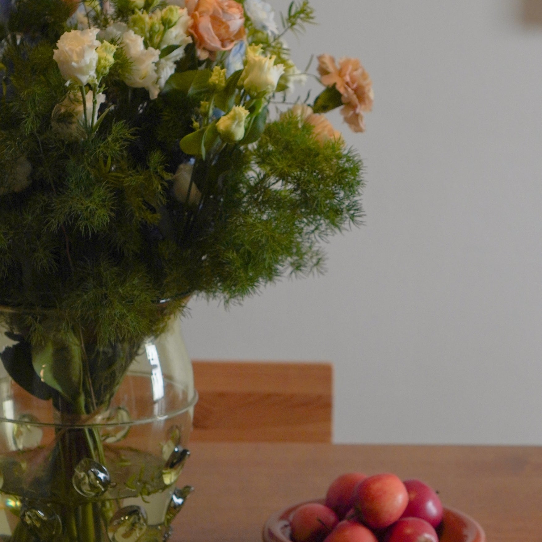 Bouquet of flowers in a glass vase on a table with a bowl of apples.