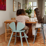Child sitting at a wooden table with olive green and grey chair in a home setting.