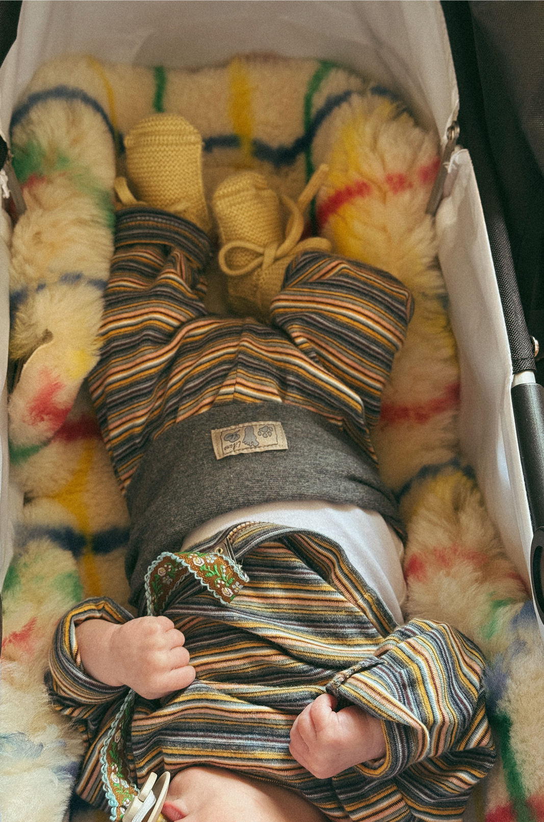Newborn baby wrapped in striped blanket with colorful yarn in background