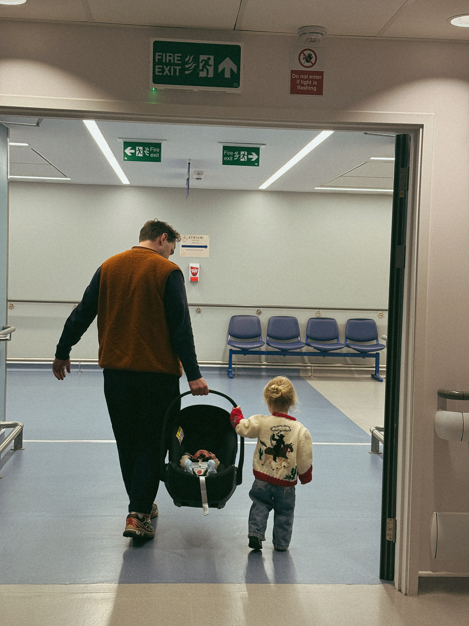 Man and child walking through a hospital corridor with a baby carrier.