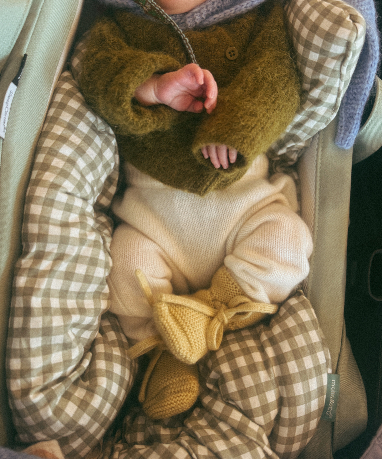 Newborn baby wrapped in checkered blanket with green sweater and yellow booties.