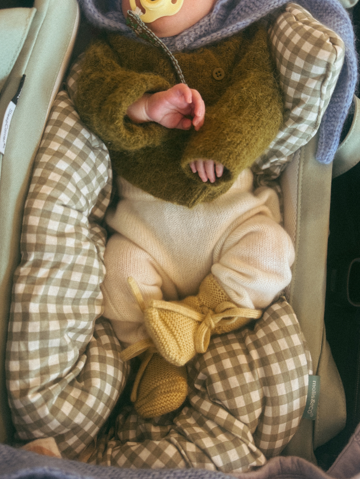 Newborn baby wrapped in checkered blanket with green sweater and yellow booties.