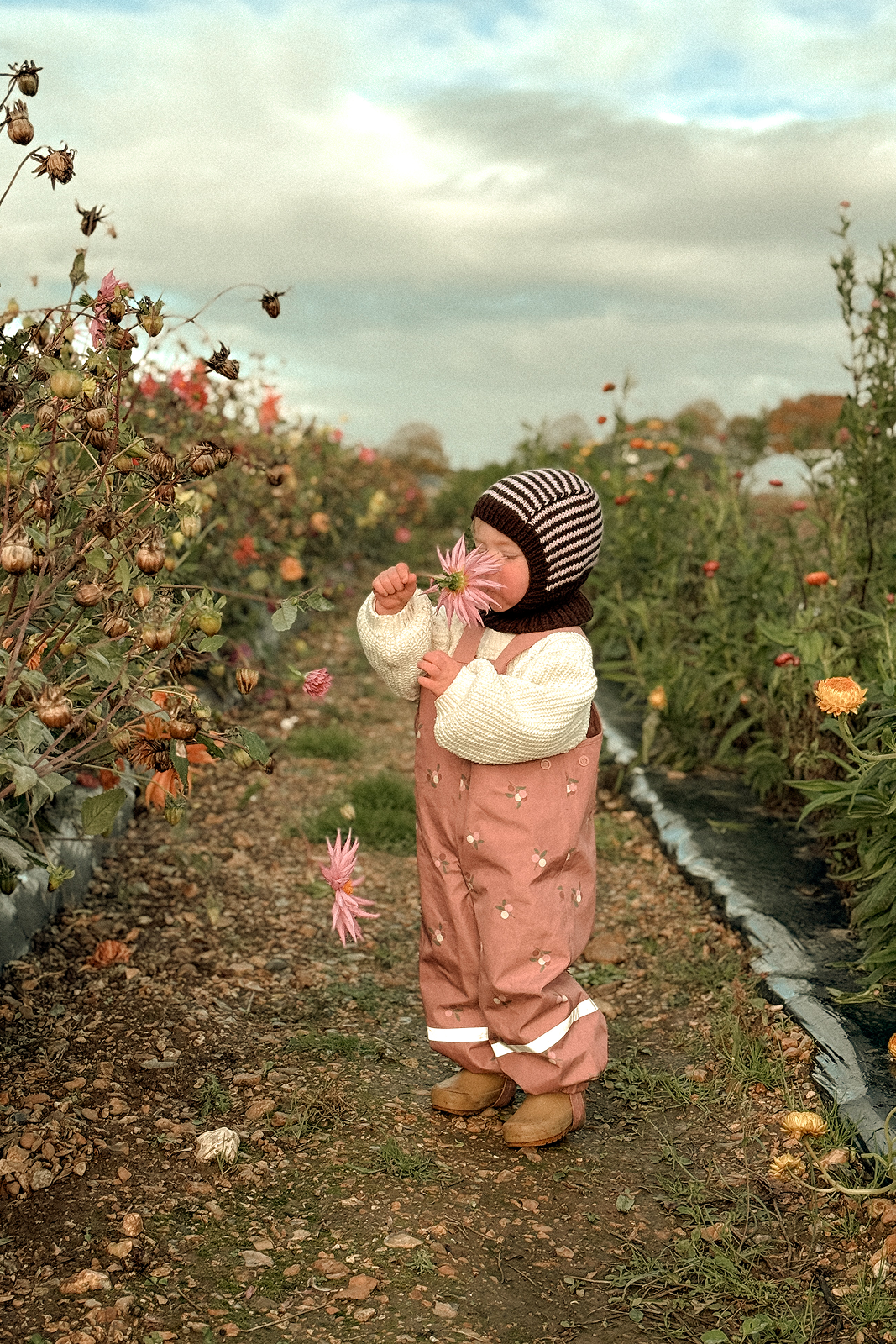 Child in a garden holding flowers with a cloudy sky in the background