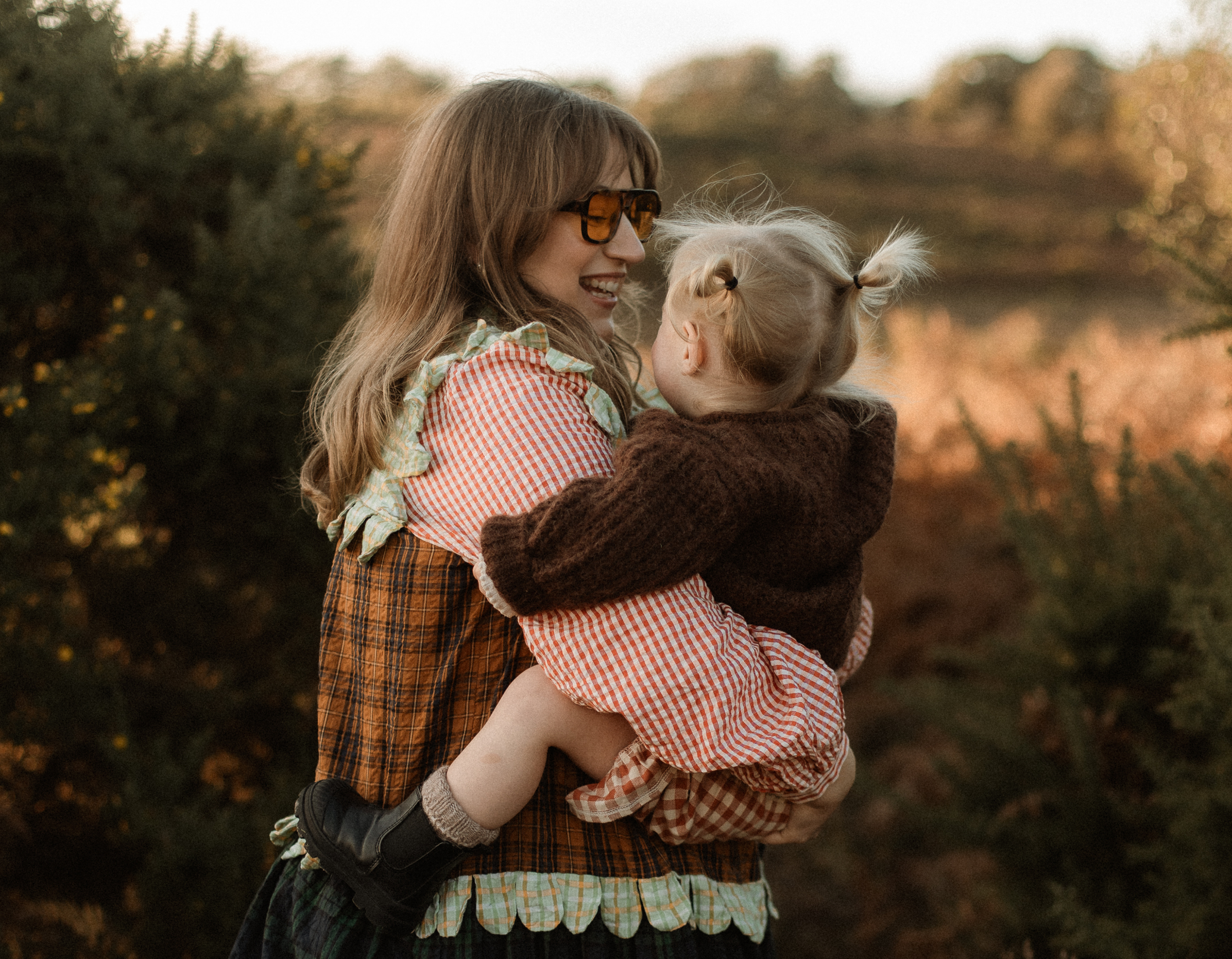 Woman holding a child in a forest during sunset