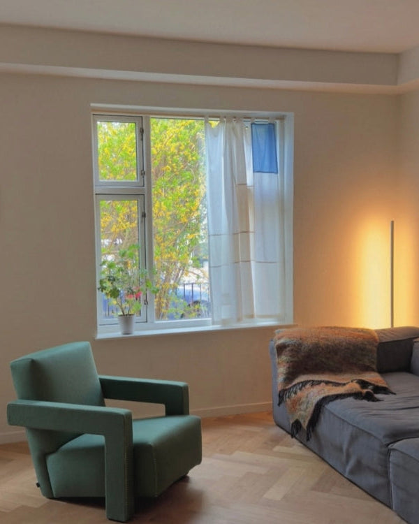 Modern living room with a green armchair and gray sofa near a window with a view of trees.