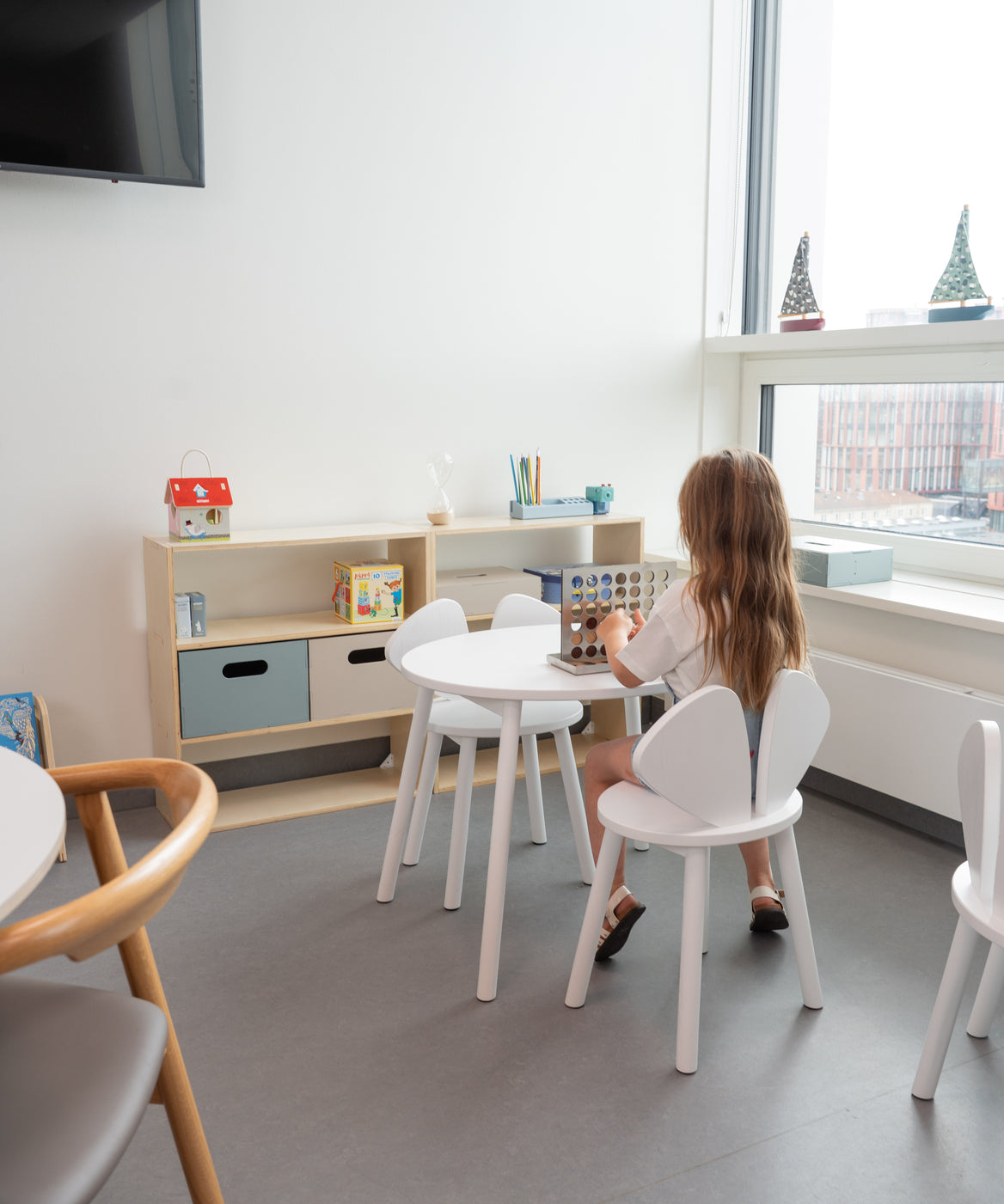 Child sitting at a table in a modern room with white chairs and a television on the wall.