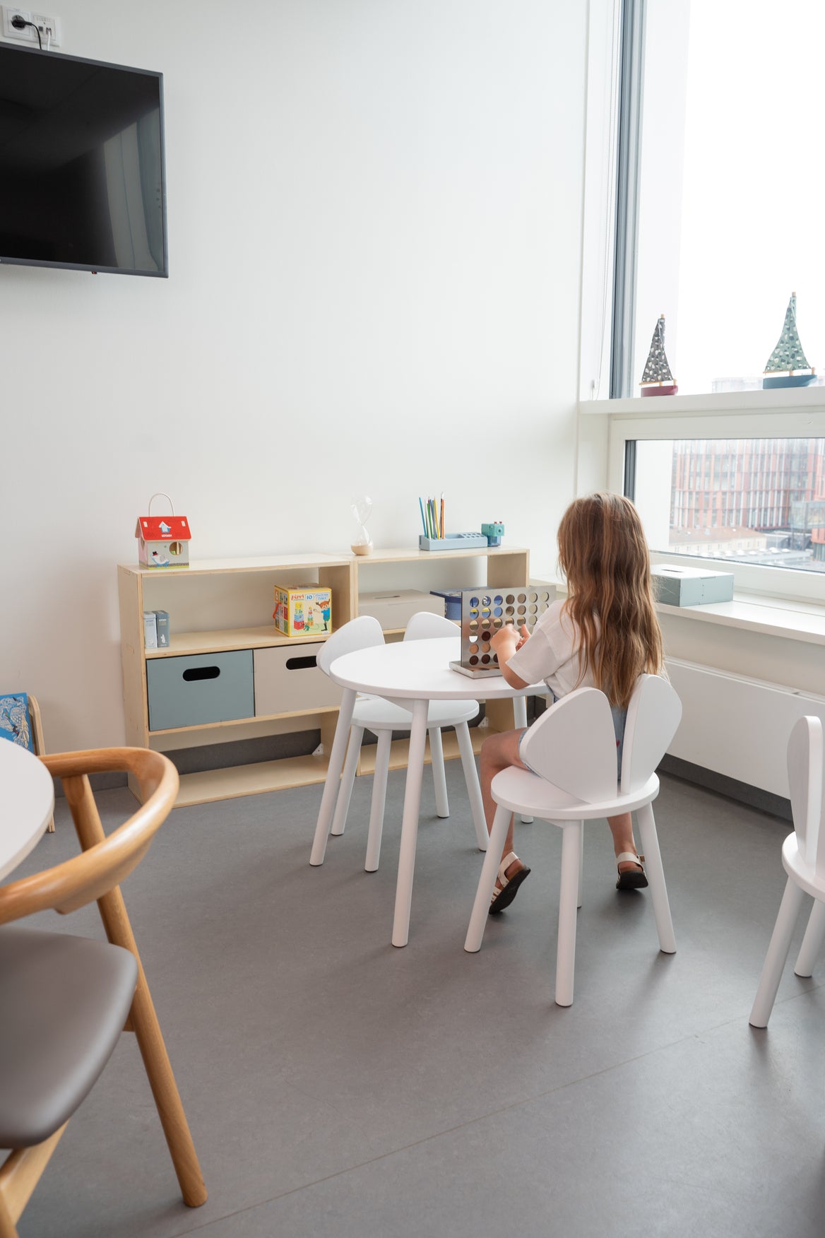 Child sitting at a table in a modern room with white chairs and a television on the wall.
