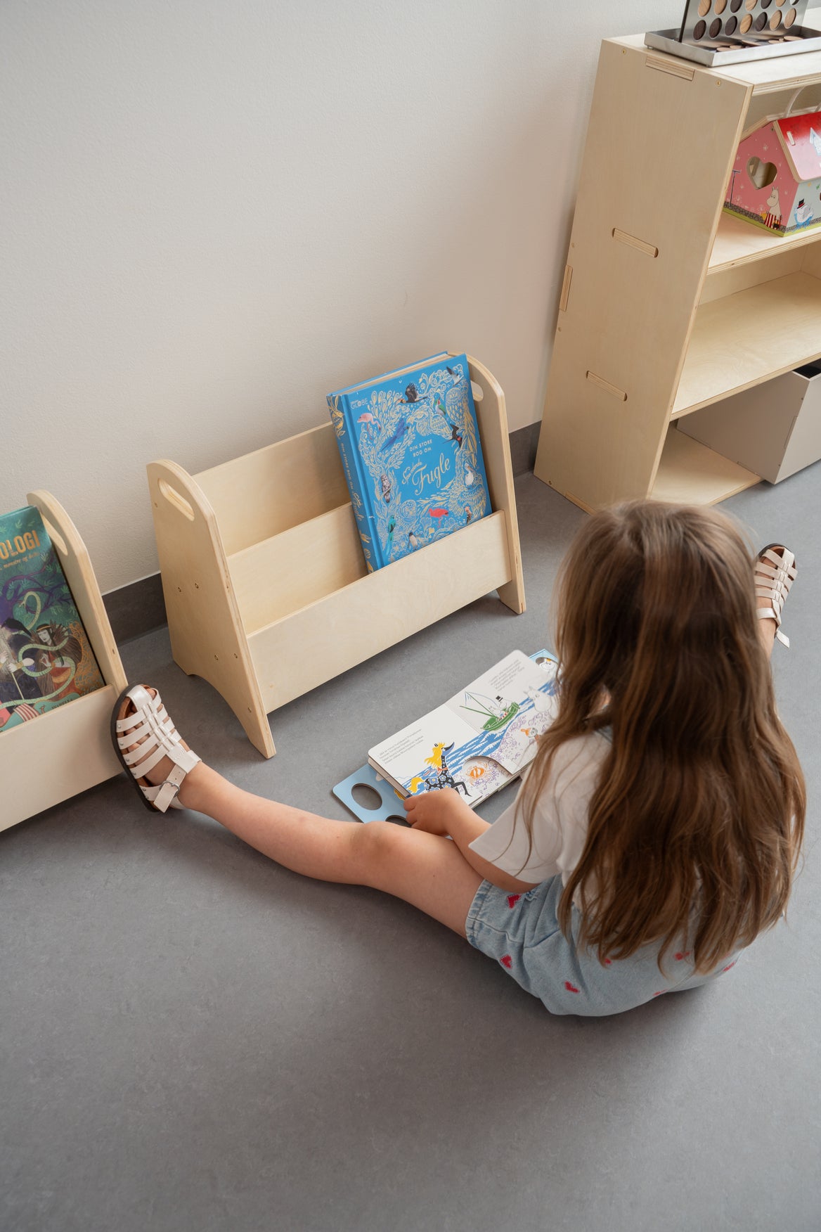 Child reading a book on the floor next to wooden bookshelves.
