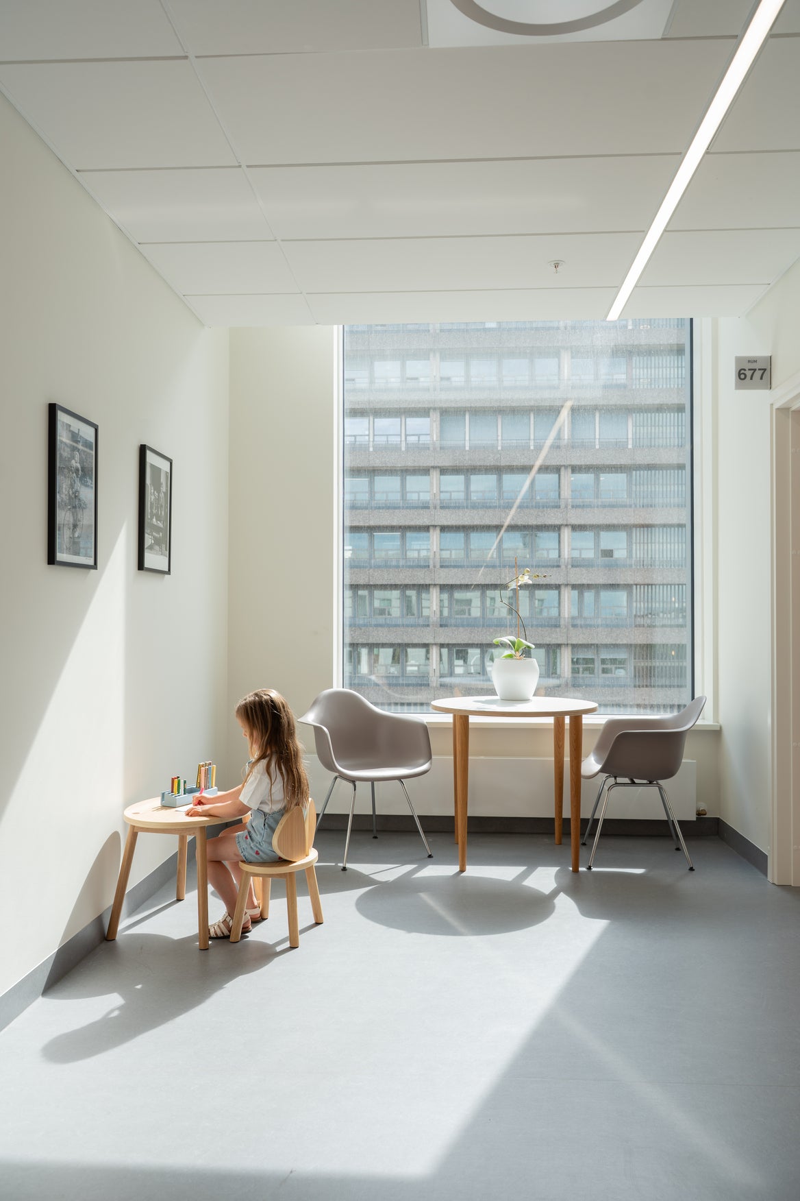 Child sitting at a small table in a bright room with large windows.