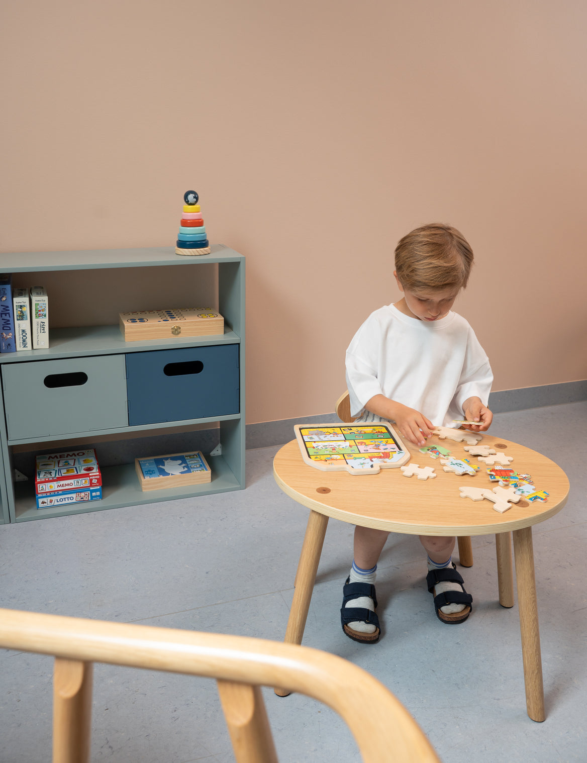Child playing with a puzzle at a small wooden table in a room with a bookshelf.