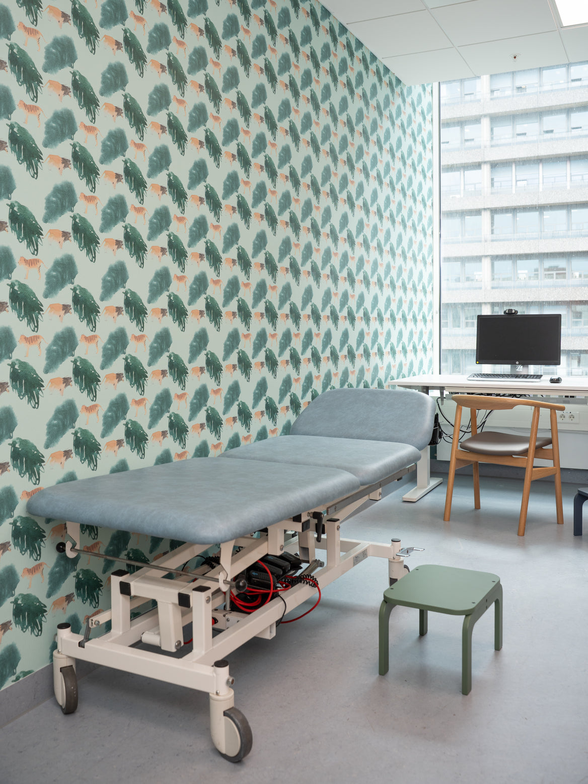 Medical examination table in a room with patterned wall and desk.