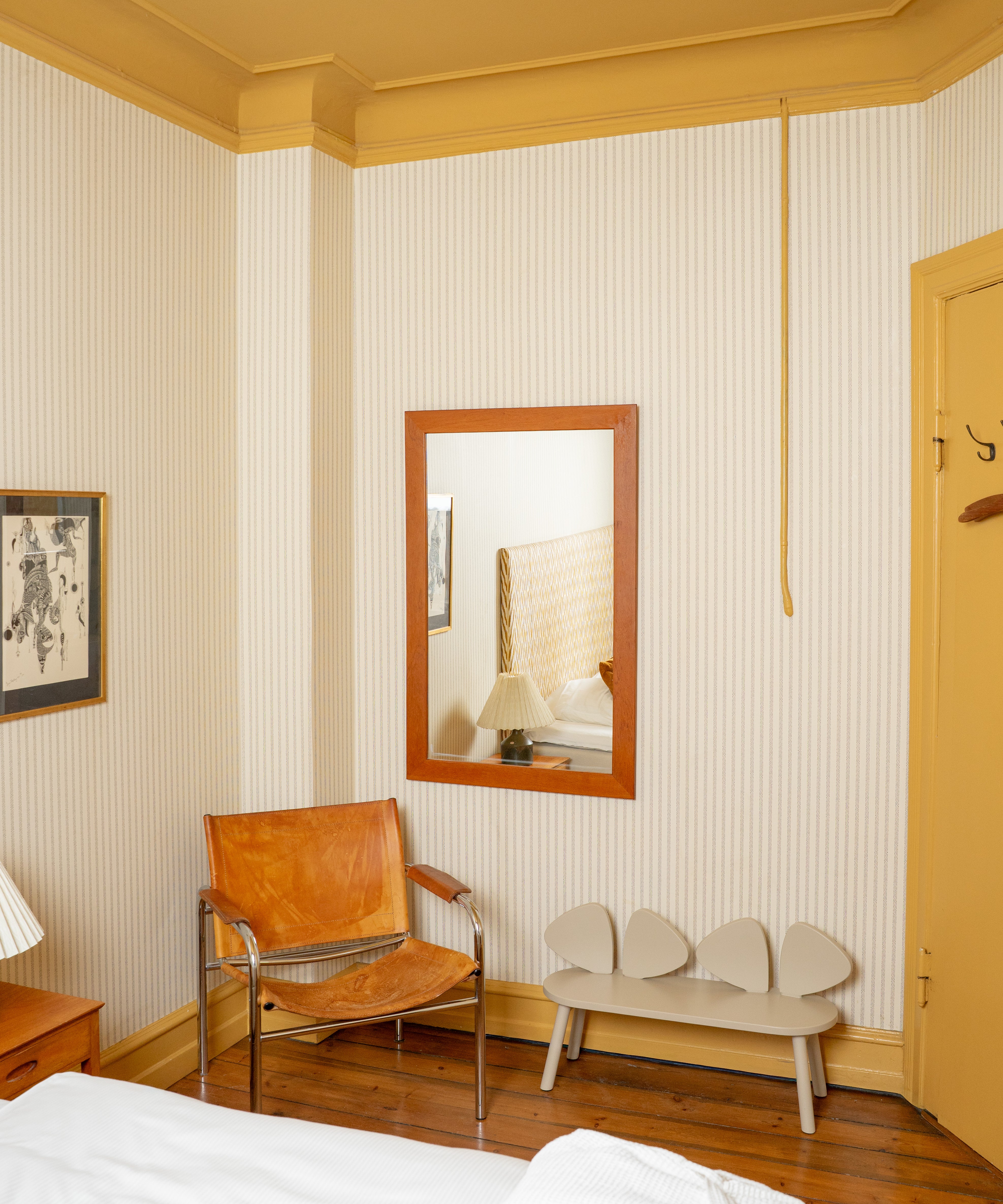 Room interior with a leather chair, mirror, and bench against striped walls.