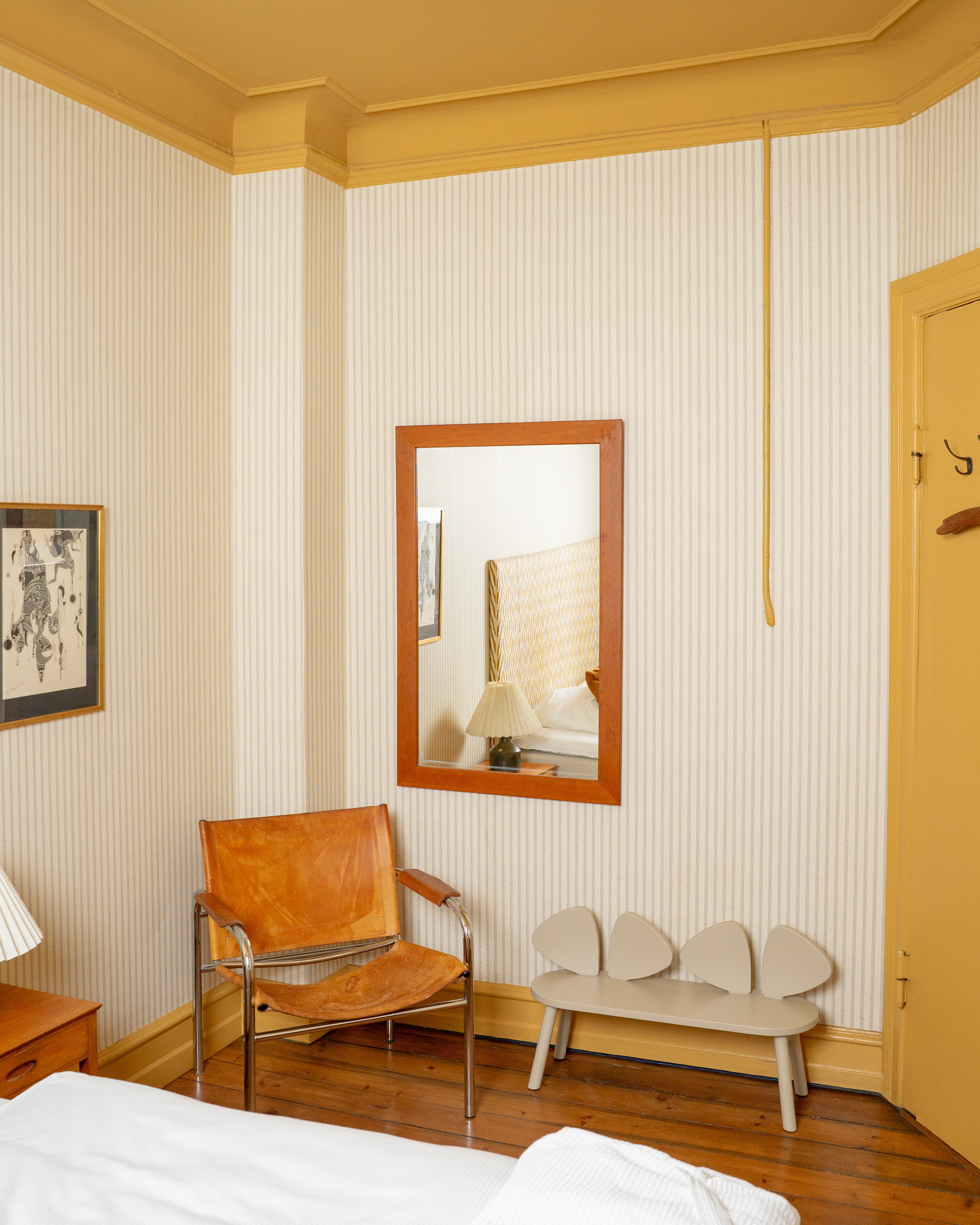 Room interior with a leather chair, mirror, and bench against striped walls.