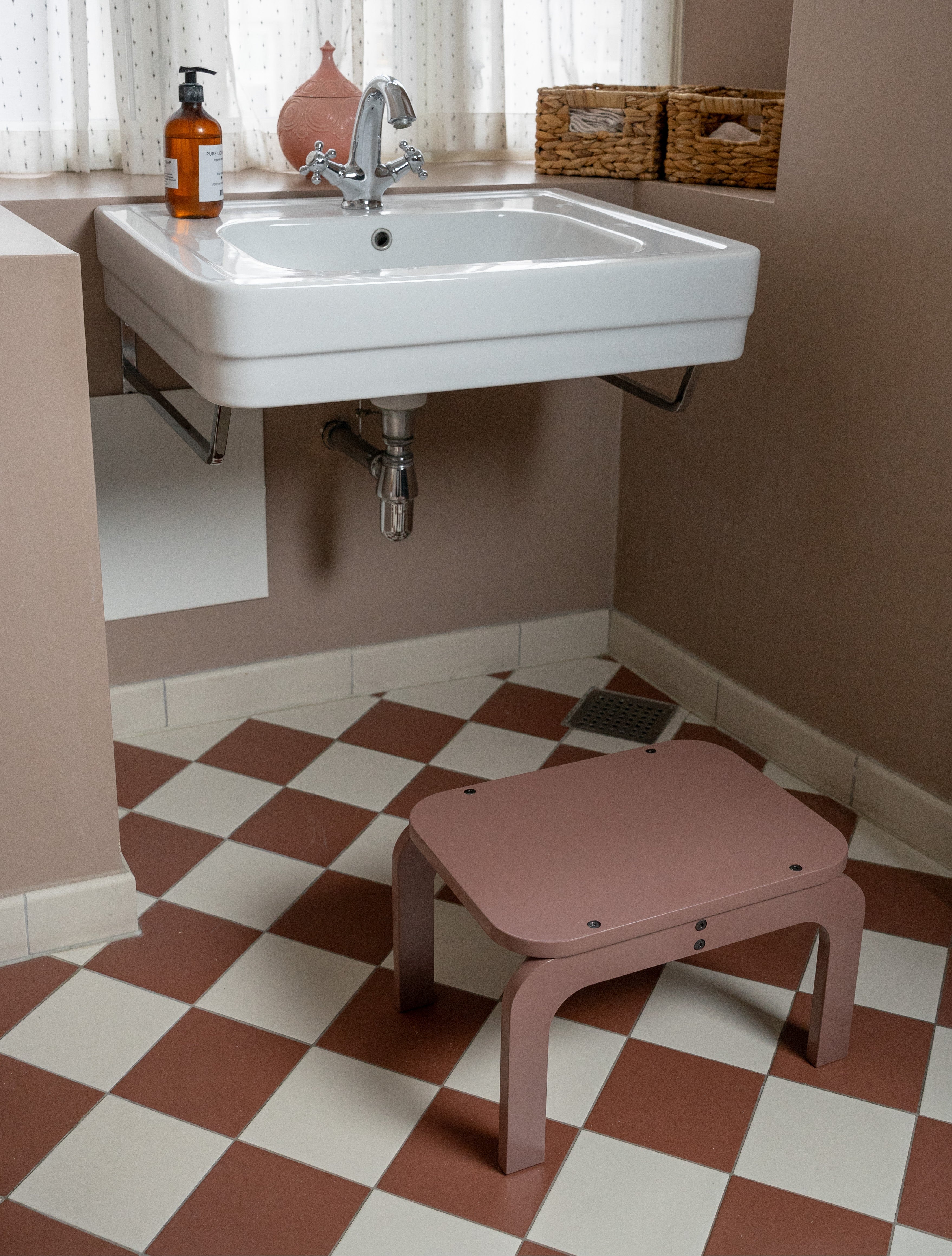 Bathroom with a white sink, checkered floor, and pink stool.