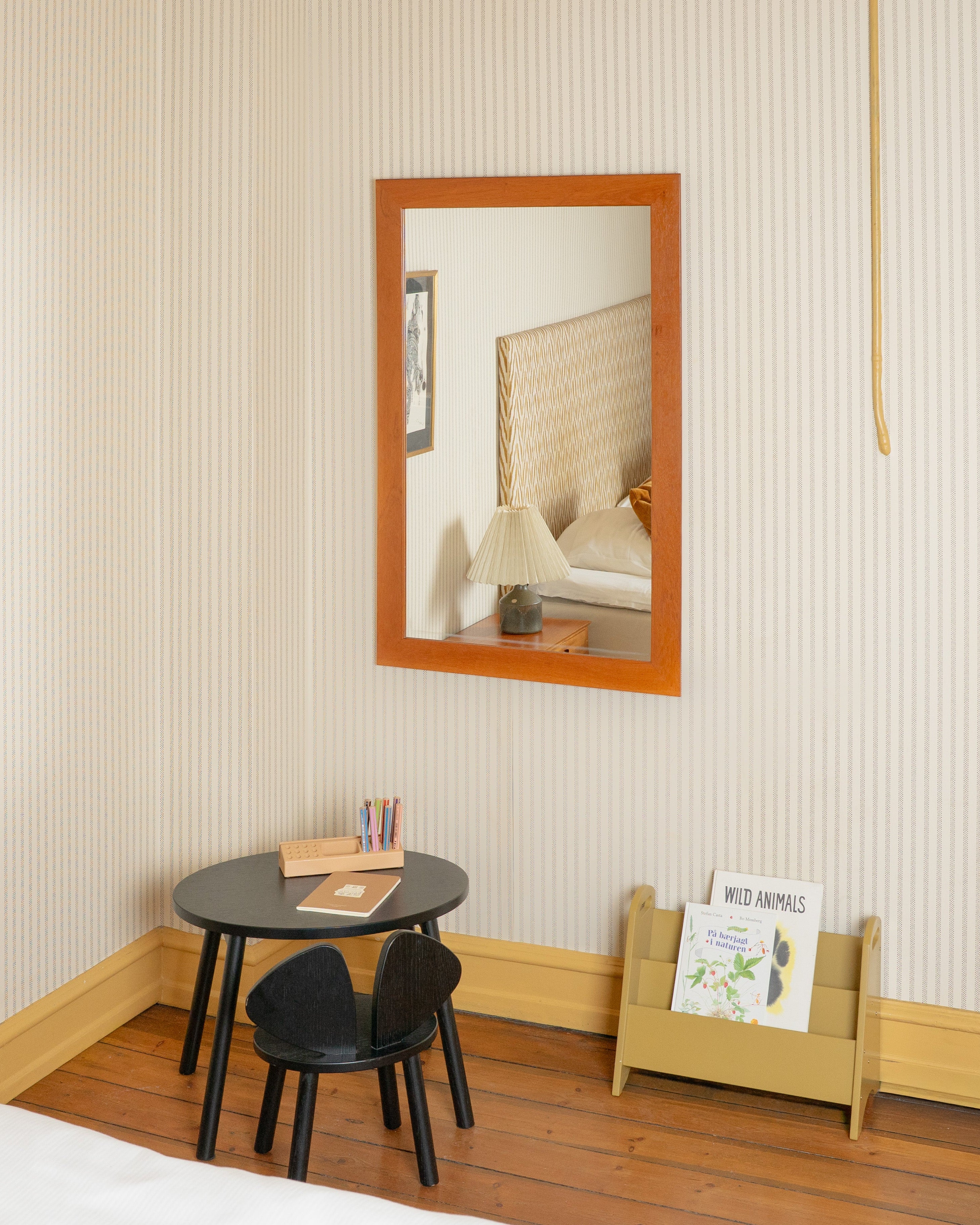 Small bedroom with striped wallpaper, bed, nightstand, mirror, and small table.