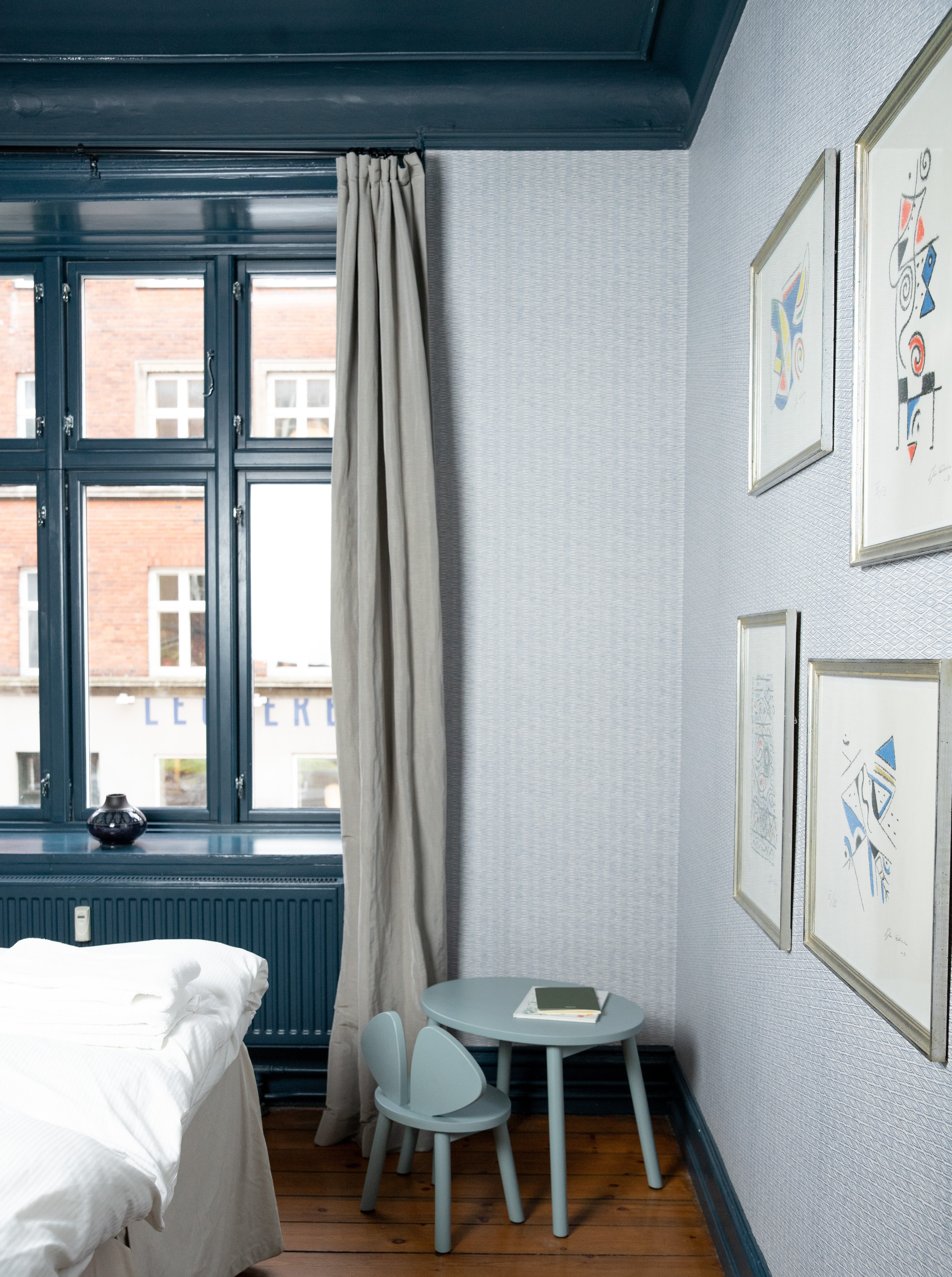Small bedroom with a bed, small table, and framed pictures on the wall.