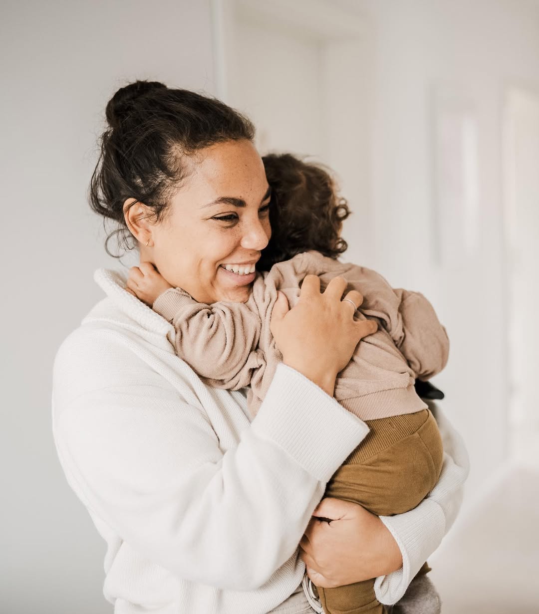Woman holding a child wrapped in a blanket against a plain background