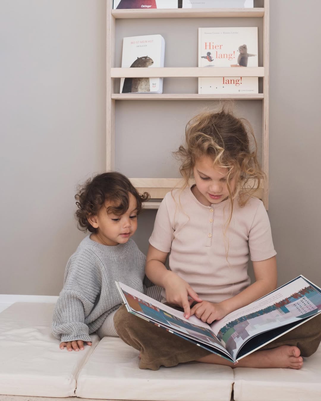 Two children sitting on a bed, looking at a book together.