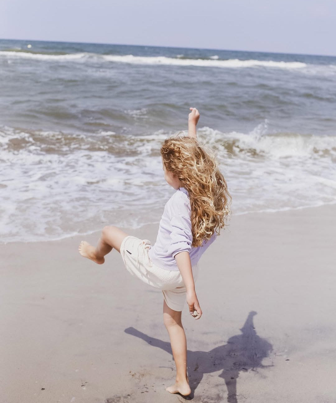 Person with long hair running on a beach with ocean waves in the background