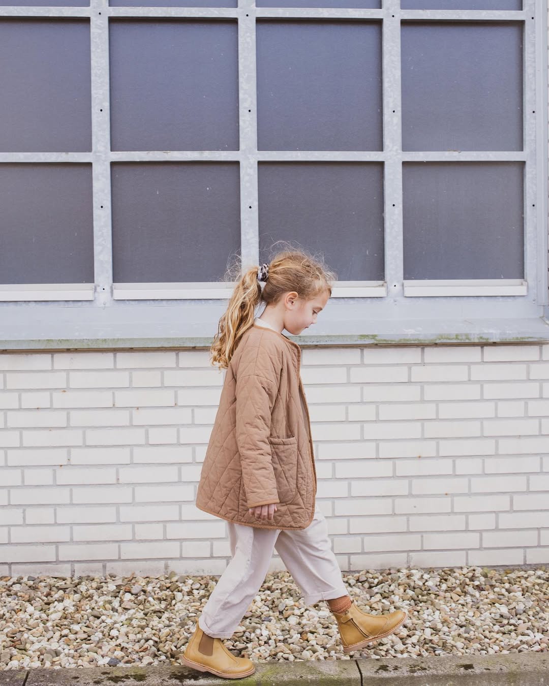 Child walking in front of a white brick wall with a gray window panel