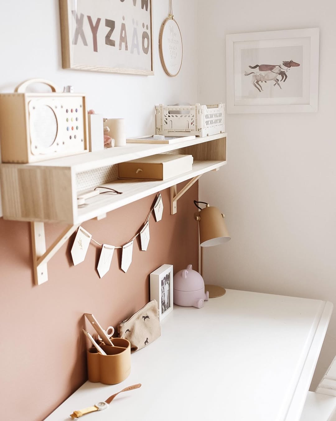 Children's play area with shelves, toys, and decorative elements on a light pink wall.