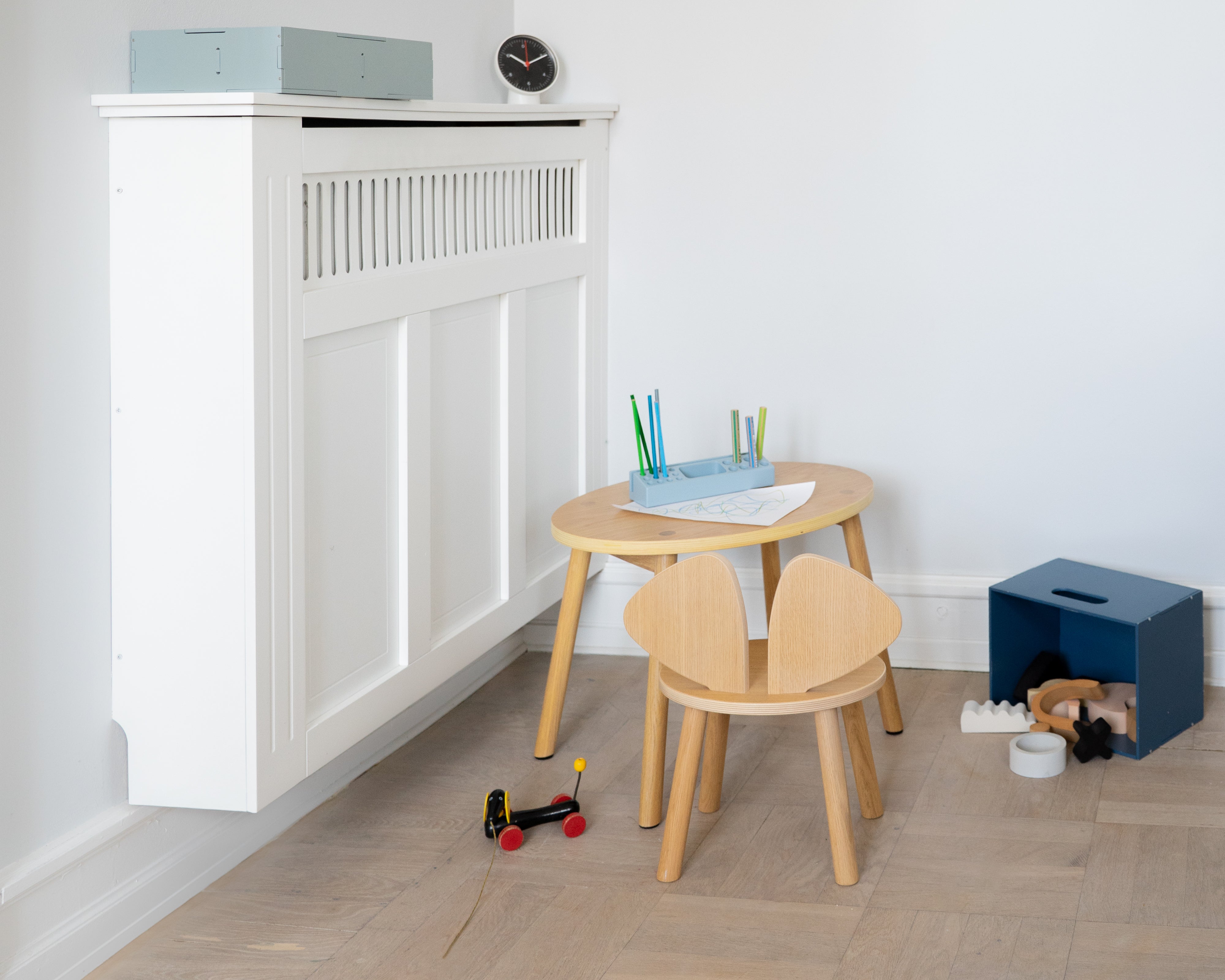 Children's play area with wooden table and chairs, toys, and a white wall.