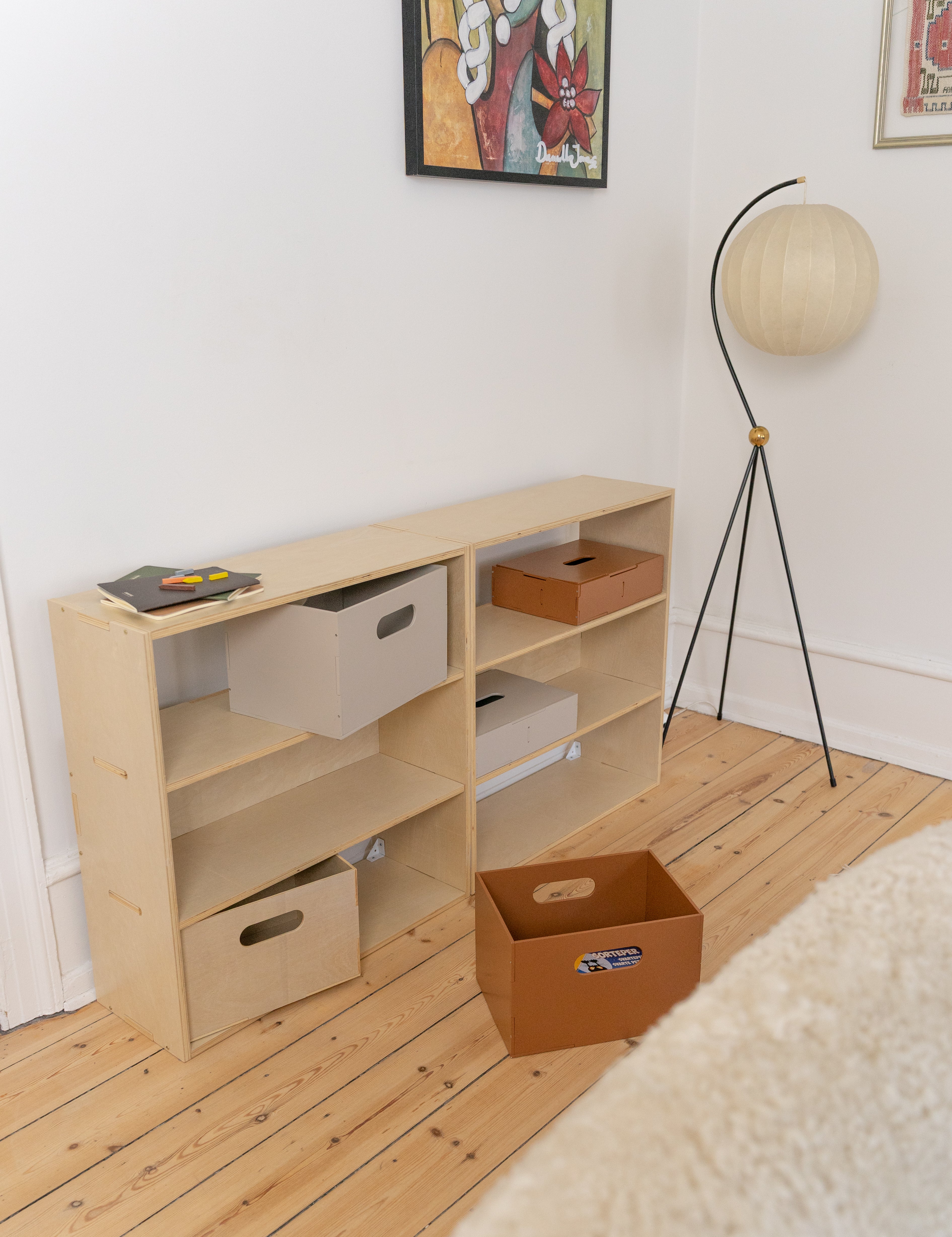 Wooden shelf with storage boxes in a room with a lamp and framed picture on the wall.