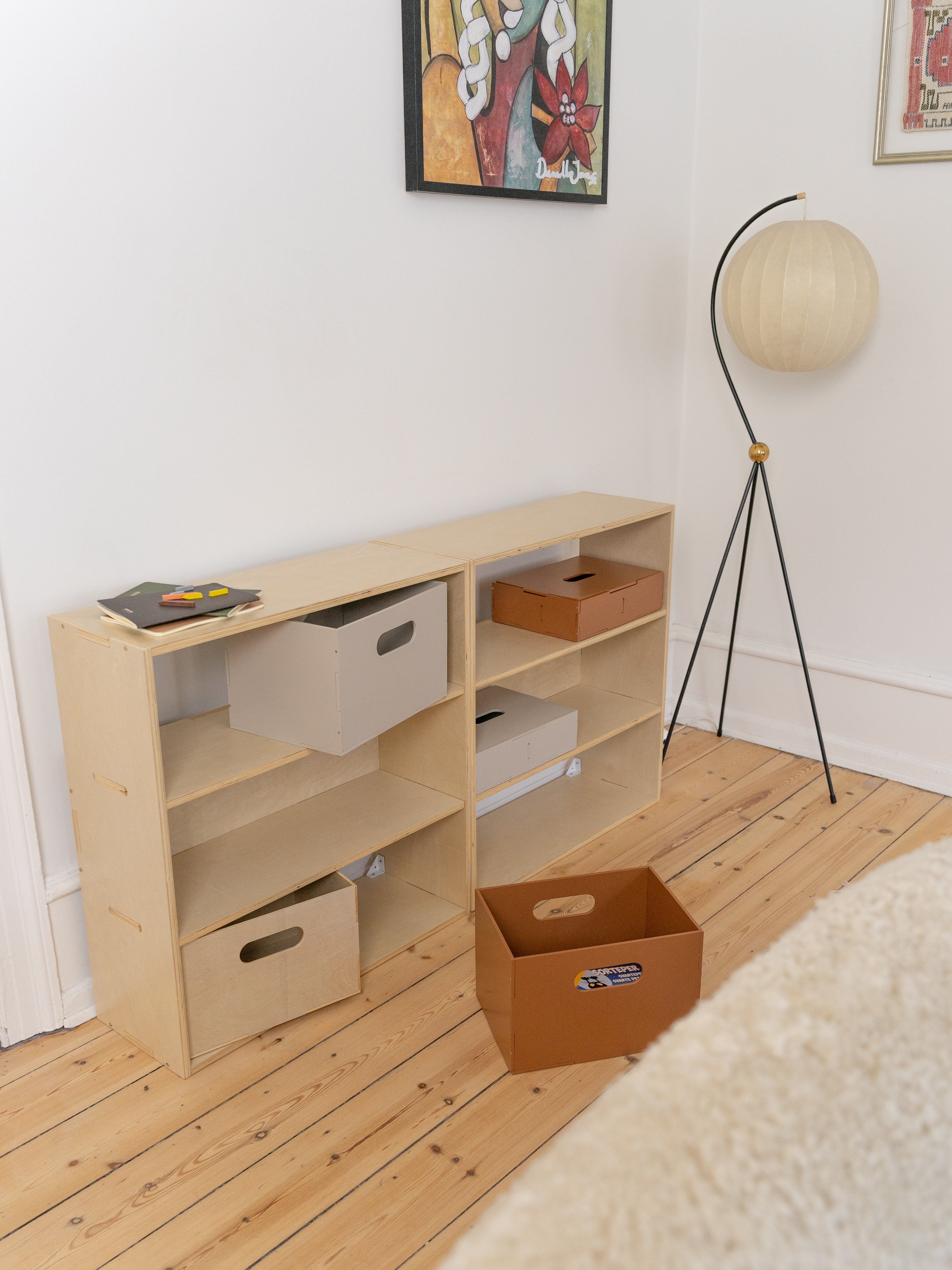 Wooden shelf with storage boxes in a room with a lamp and framed picture on the wall.