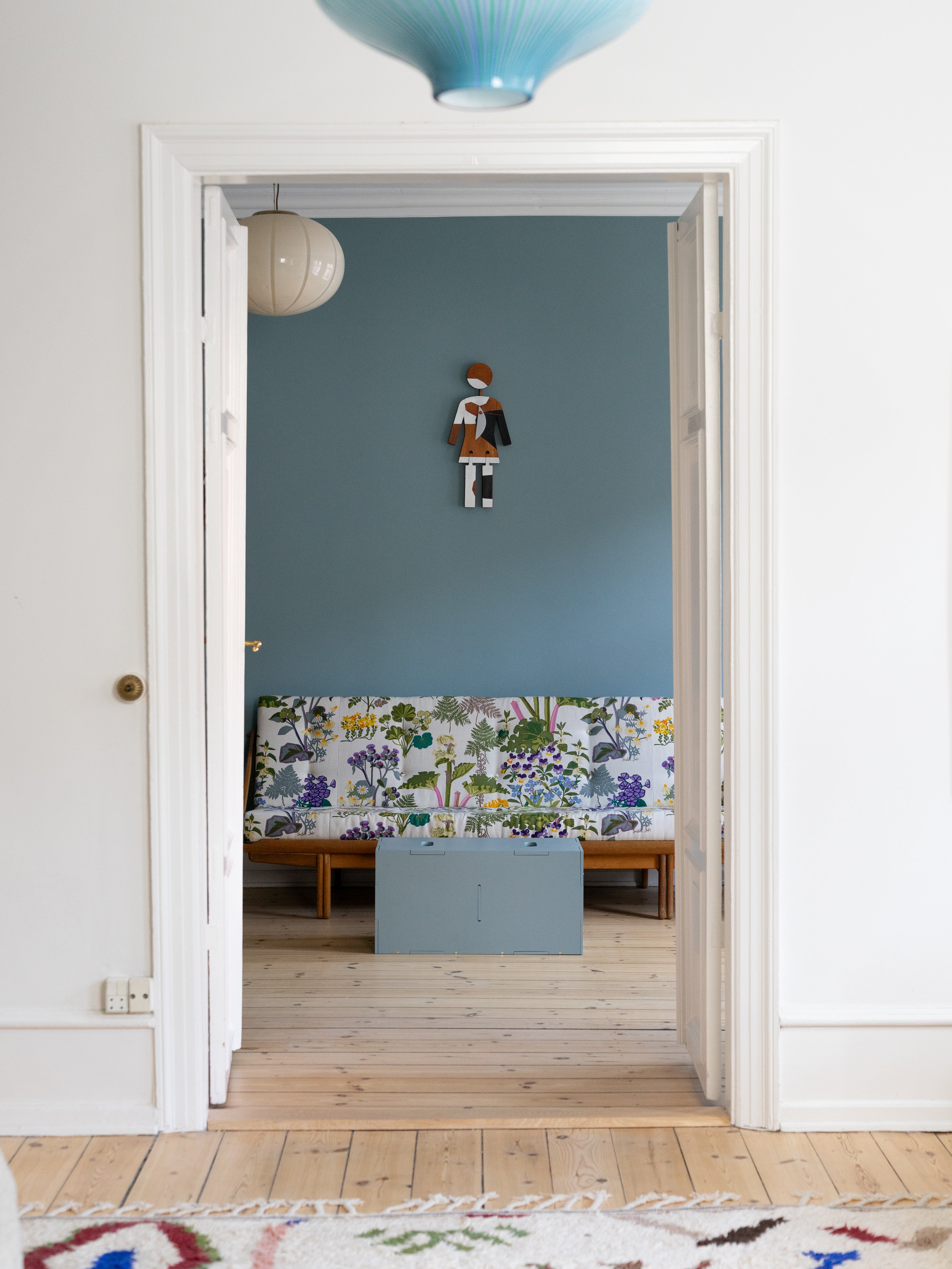 View of a room with a blue wall, colorful wallpaper, and wooden floor.
