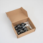 An open brown cardboard box containing four black caster wheels with metal axles and a small clear bag of hardware, photographed on a clean light gray studio background.