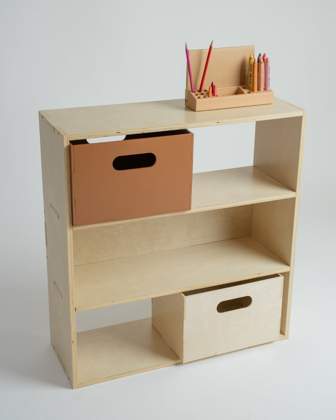 A light natural wood open shelving unit with three tiers, styled with storage boxes and a pencil holder on top, set against a plain light gray background.