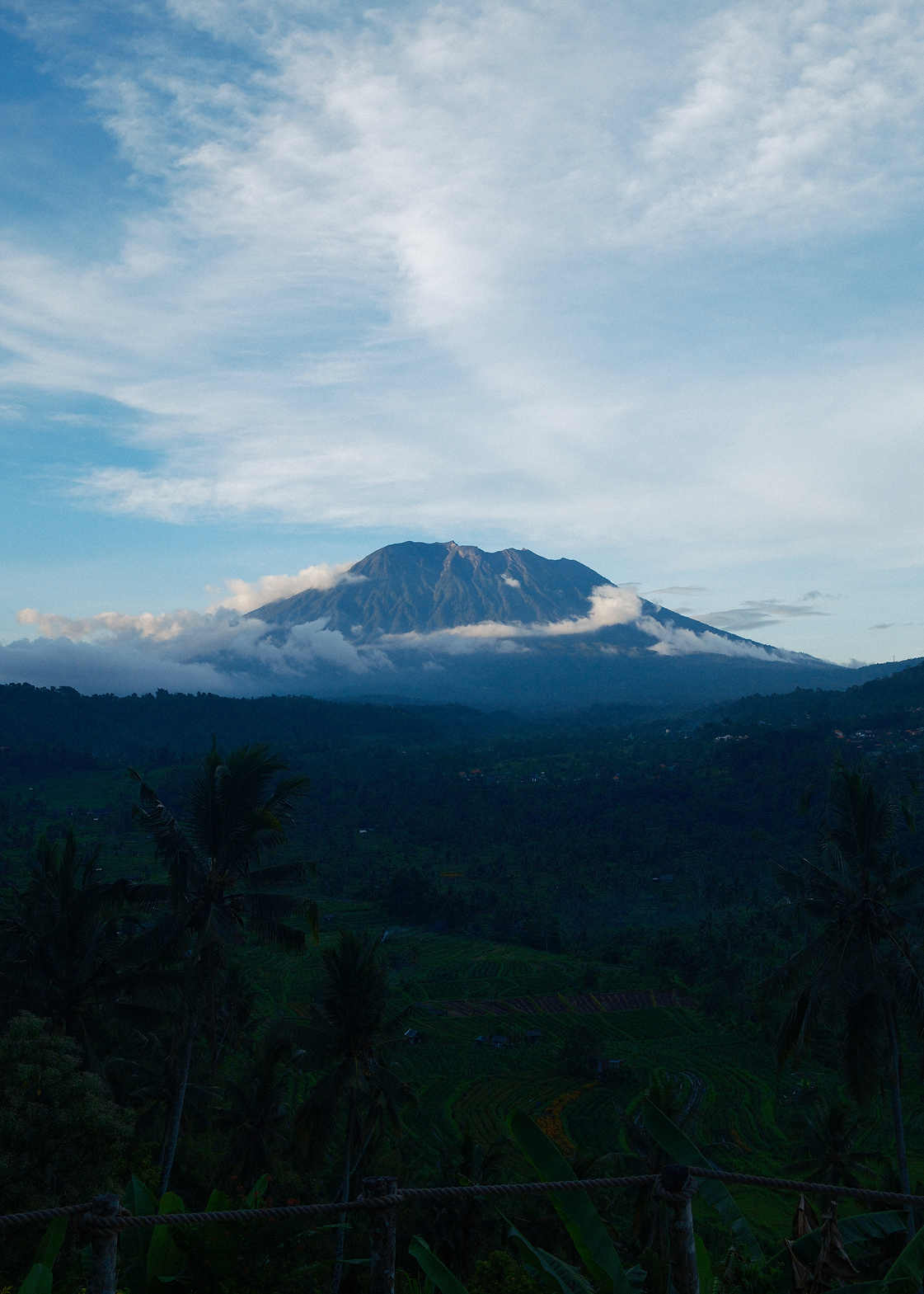 Mountain peak with clouds in a blue sky over a forested landscape