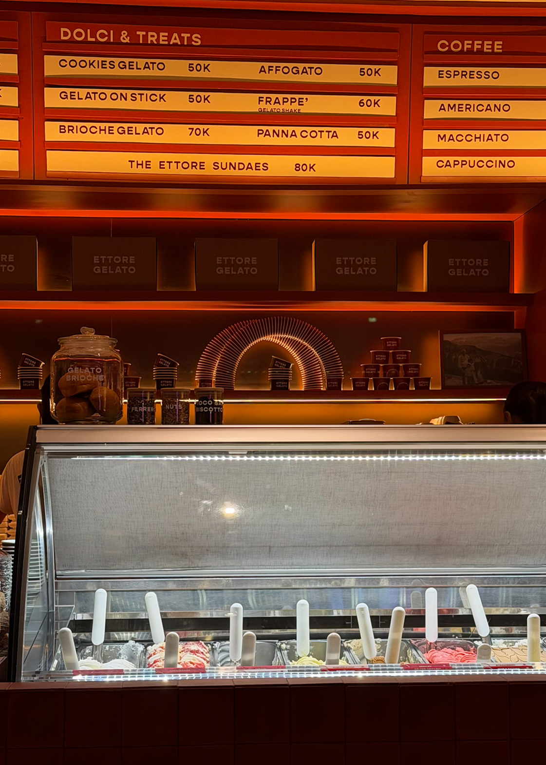 Ice cream display case with menu board behind, featuring Dolci & Treats and coffee options.