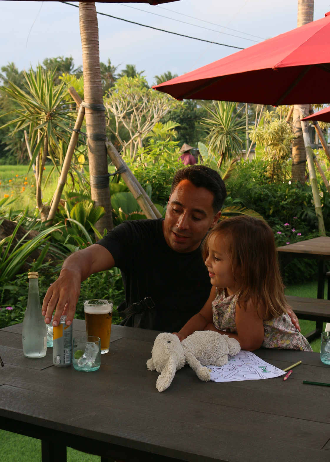 Man and child at a table with drinks and a teddy bear in a garden setting