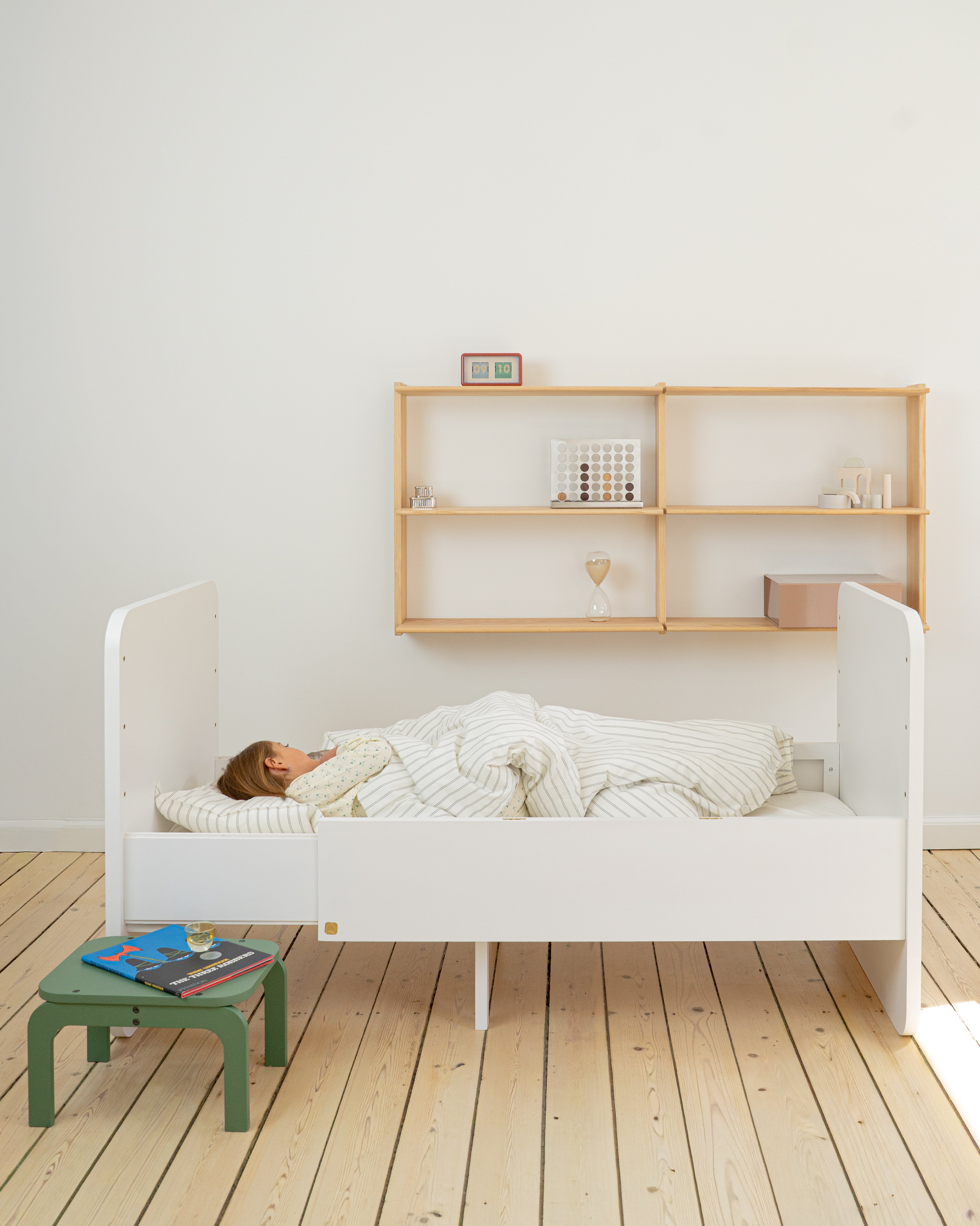 Person lying in a white bed with wooden shelves in the background