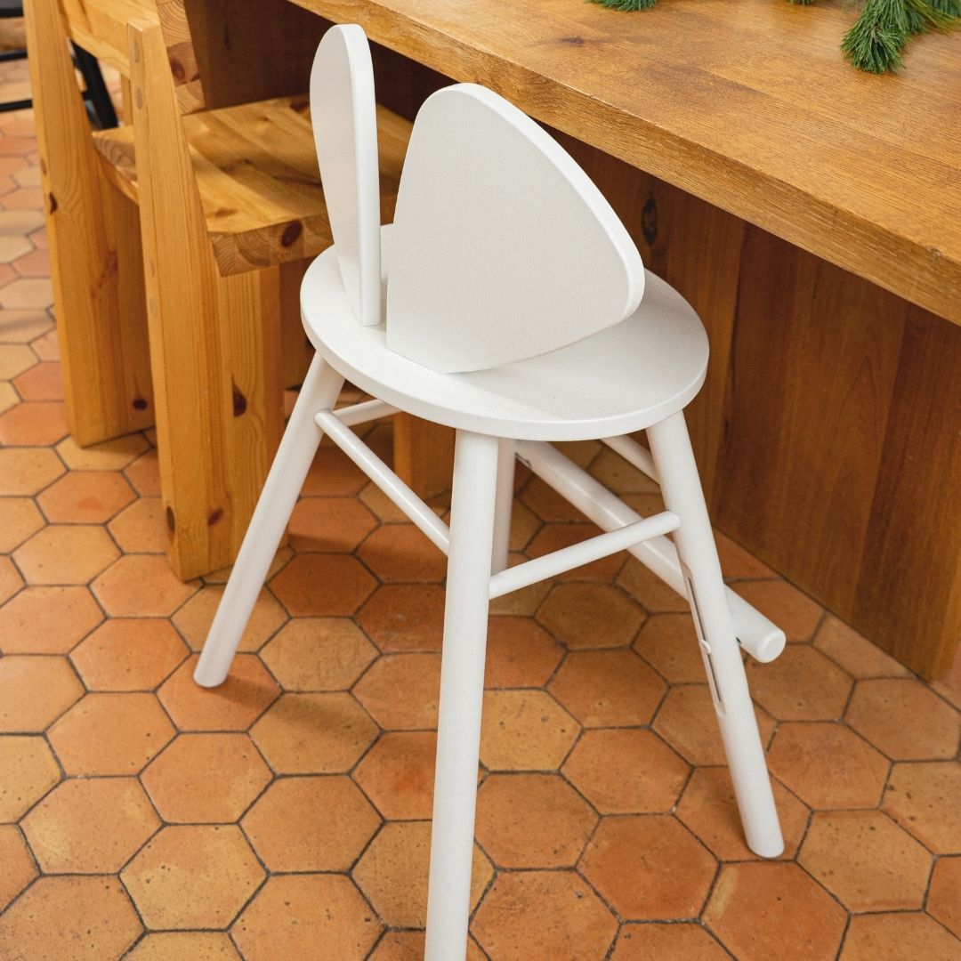 White junior mouse stool in front of a wooden counter on a terracotta tiled floor.