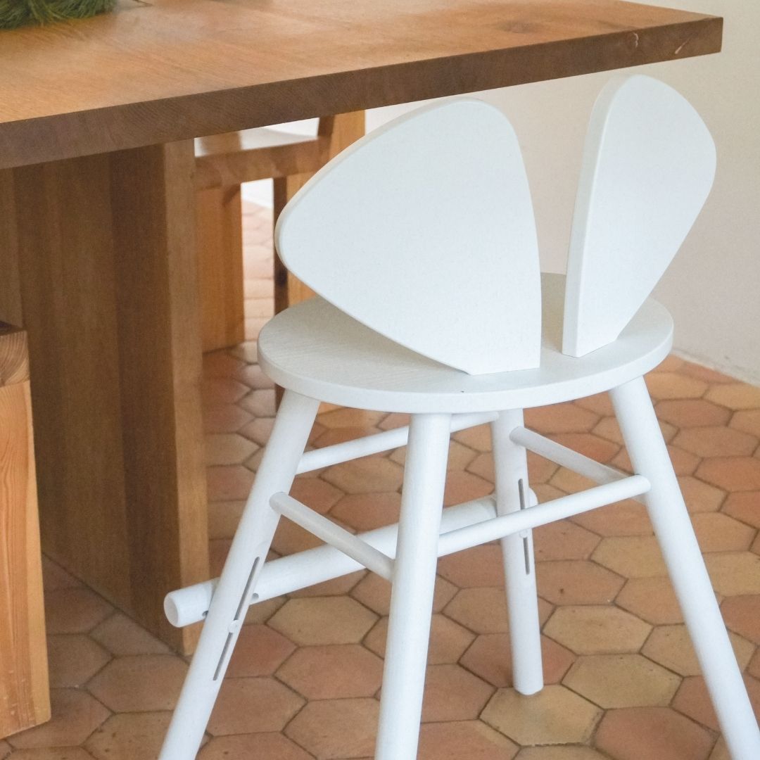 White Junior Mouse chair with a unique design next to a wooden table on a terracotta tiled floor.